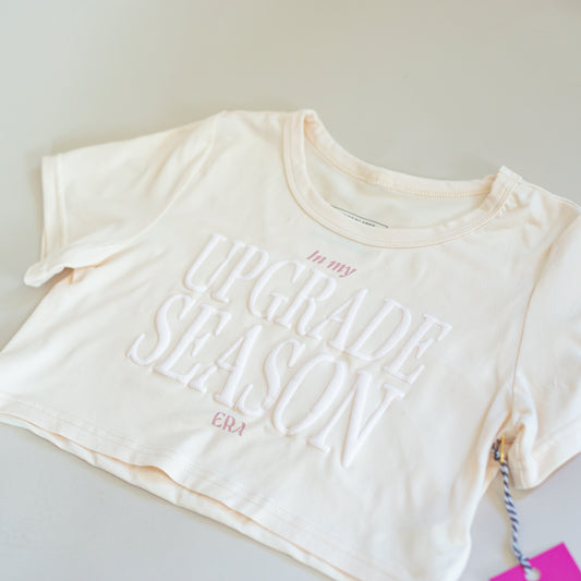 Beige crop top with 'In my Upgrade Season' text by CBC Sportswear. Made from soft, comfortable fabric, perfect for active wear. Ideal for young athletes and gymnasts looking for stylish and motivational apparel."