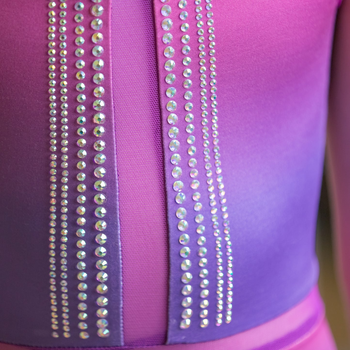 Close-up of sparkling linear design on the front of the purple and pink Linear Leo gymnastics leotard by cbcsportswear. Features shimmering rhinestone accents for a stylish and eye-catching look. Perfect for young gymnasts.